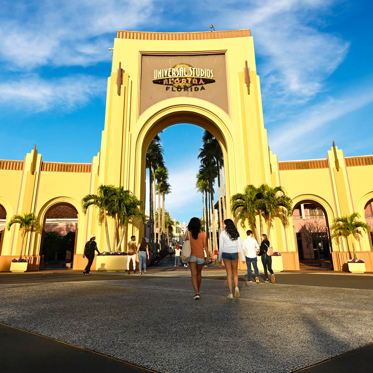 Visitantes caminham em direção ao arco de entrada do Universal Studios Florida sob o céu azul.