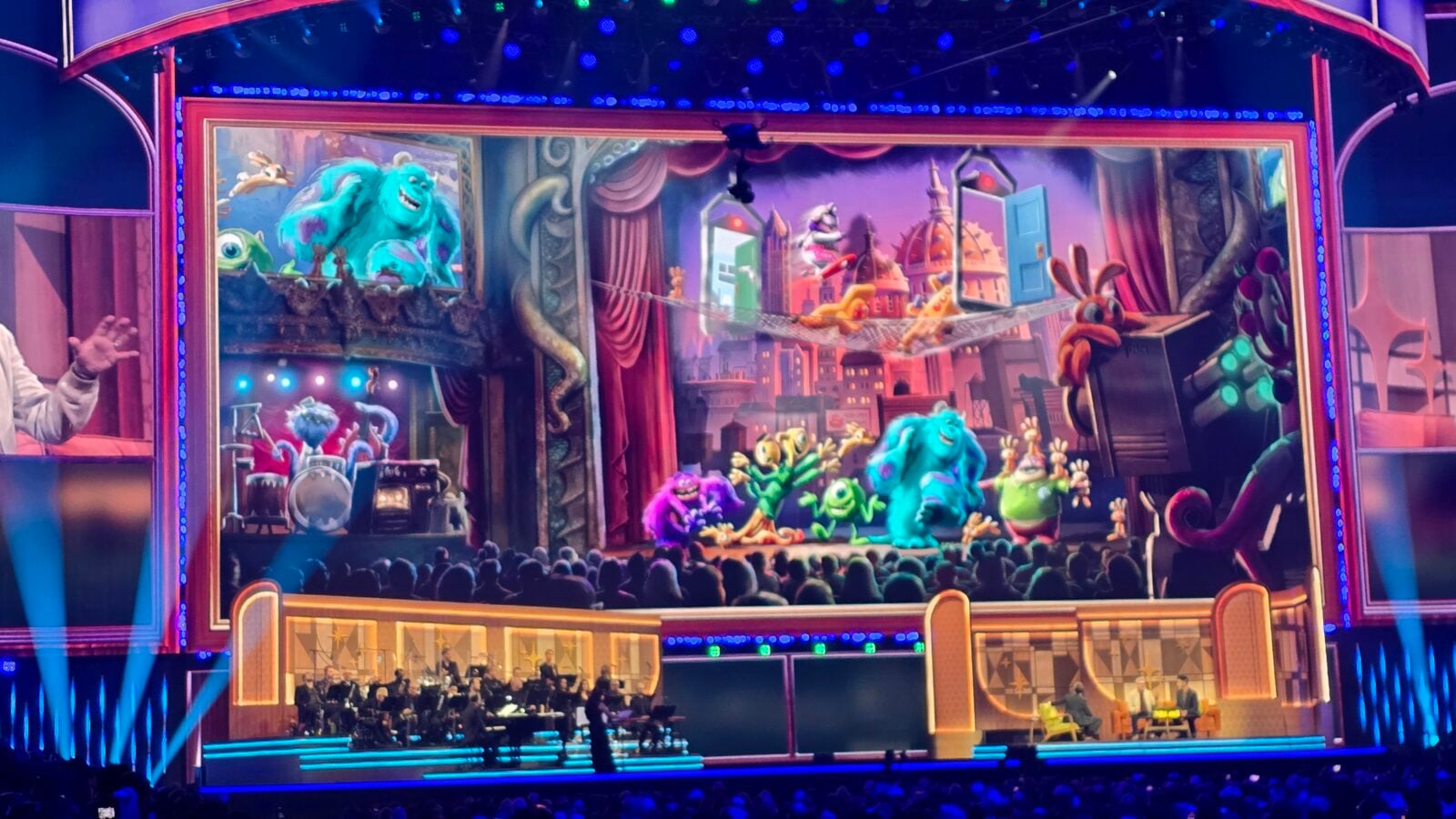 Palco do Horizons com arte de Monstropolis no telão, personagens, apresentadores e orquestra.