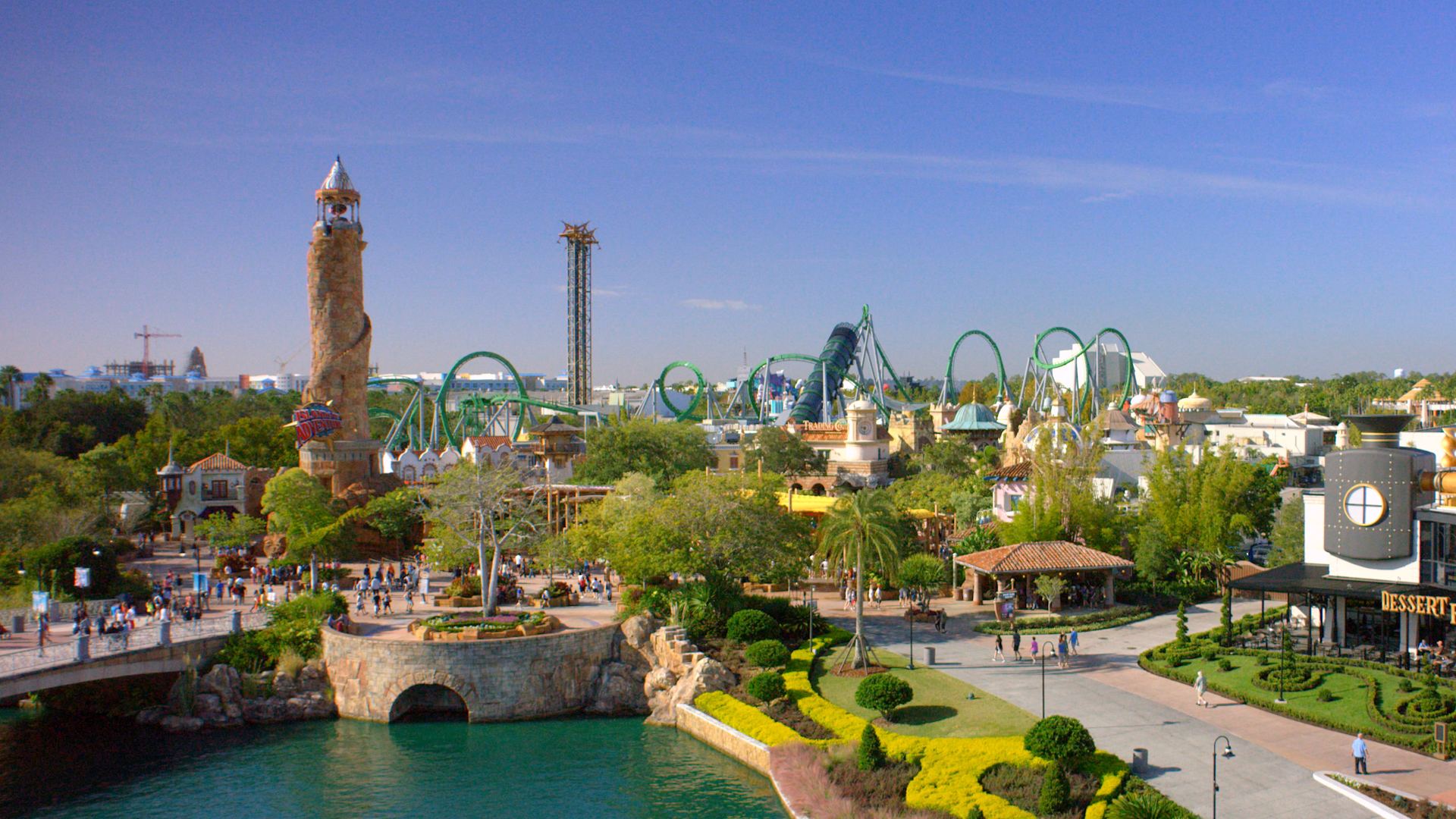 Vista panorâmica do Islands of Adventure com a torre de entrada, o lago e montanhas-russas ao fundo.