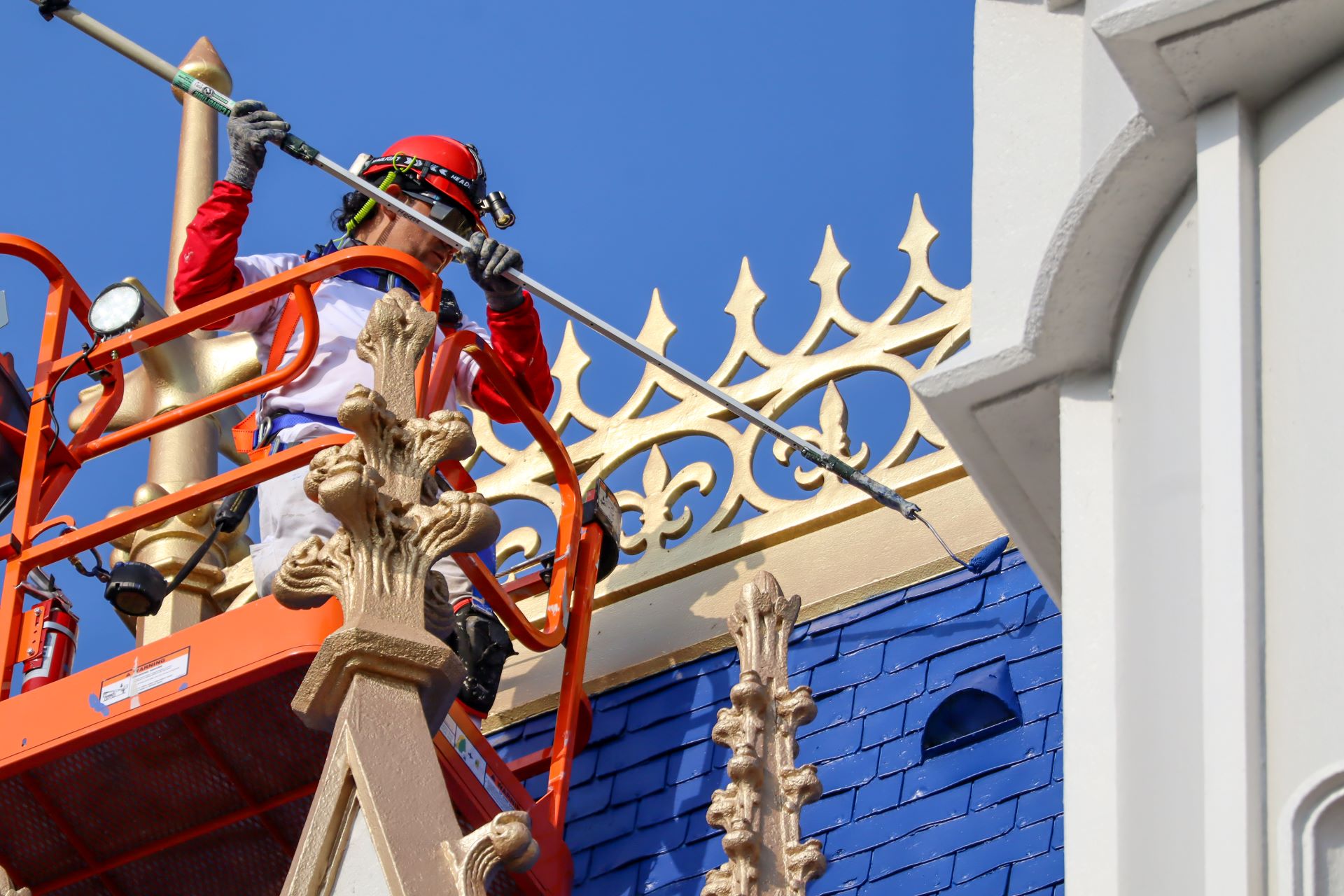 Profissional pinta detalhes dourados do Castelo da Cinderela em uma plataforma elevatória.