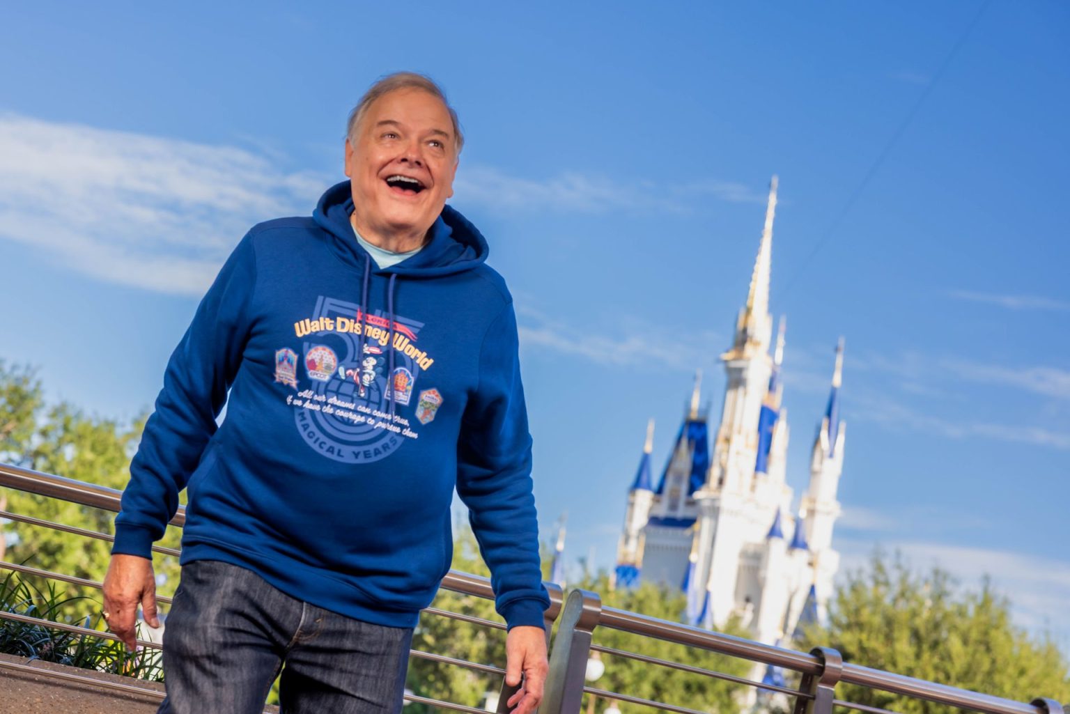 Cast Member do Walt Disney World desde 1971 usa blusa comemorativa diante do Castelo da Cinderela.